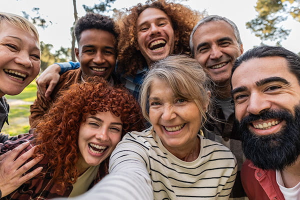 Group of cheerful, multi-ethnic friends spanning various ages smiling and taking a selfie in a park setting