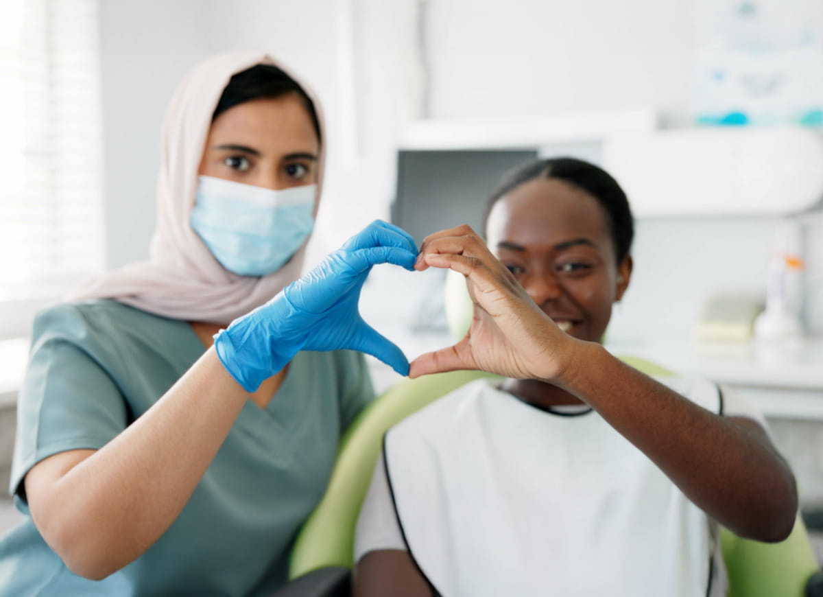 Patient and nurse smiling while forming a heart shape with their hands.