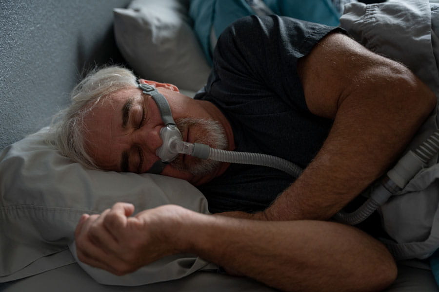 Older man sleeping in his bed wearing a CPAP mask