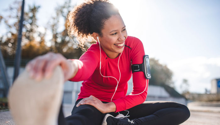 Young woman outside sitting on the ground stretching before exercising. 