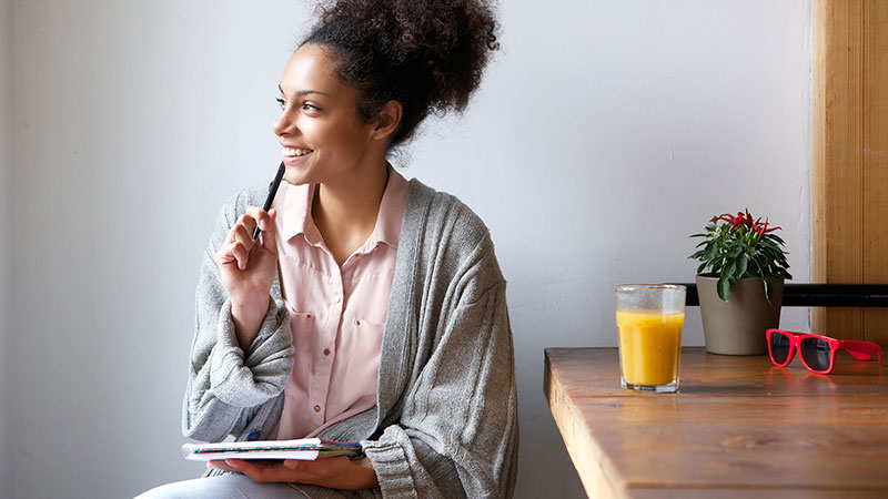 mujer afroamericana en pijama sonriendo mientras escribe su diario