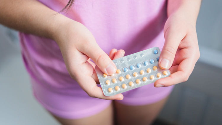 Una mujer joven, vestida con un pijama de color rosa, sostiene sus píldoras anticonceptivas.