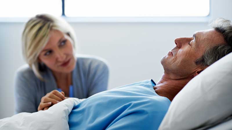 mujer sentada junto a su esposo en la cama del hospital